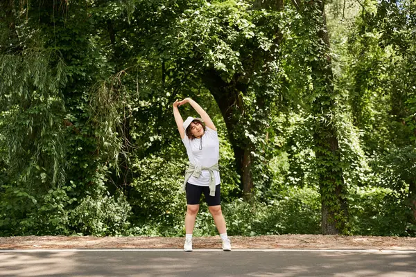 A pretty young woman enjoys an outdoor workout by stretching in a vibrant park filled with greenery. — Stock Photo