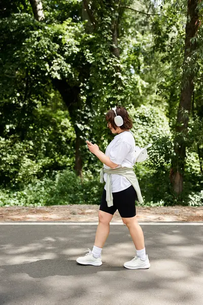 Uma jovem caminha por um caminho sereno, com fones de ouvido ligados, imersos na música e na natureza. — Fotografia de Stock