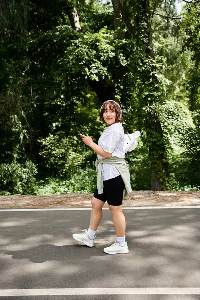 A pretty young woman strolls in the sun, enjoying a lovely summer day surrounded by greenery. — Stock Photo
