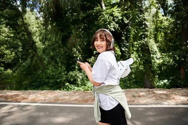 Bright summer day brings joy as a young woman listens to music while walking in nature. — Stock Photo
