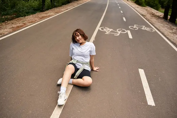 A young woman sits on the pavement under the sun, enjoying a peaceful summer day outdoors. — Stock Photo