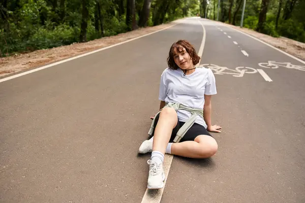 Uma jovem se senta em uma ciclovia, abraçando o calor do verão e a tranquilidade da natureza. — Fotografia de Stock