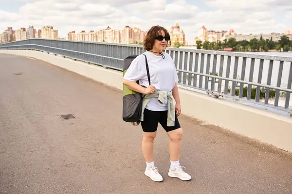 Fit woman dressed for exercise walks along a riverside path in a vibrant urban setting. — Stock Photo