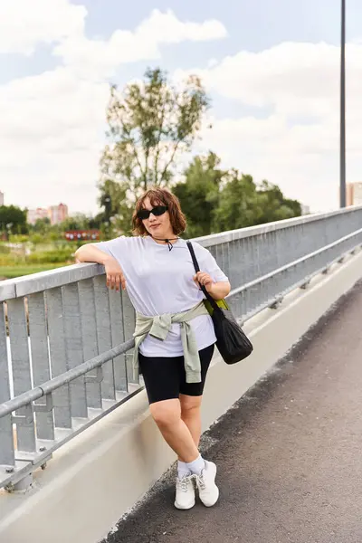 Una donna in forma si appoggia a una ringhiera ponte, godendo il suo allenamento all'aperto all'aria aperta. — Foto stock