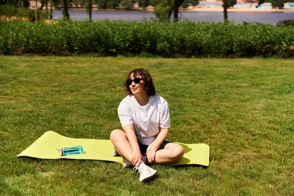 Una giovane donna felice si rilassa su un tappetino yoga vicino a un lago panoramico, godendo di fitness all'aperto. — Foto stock