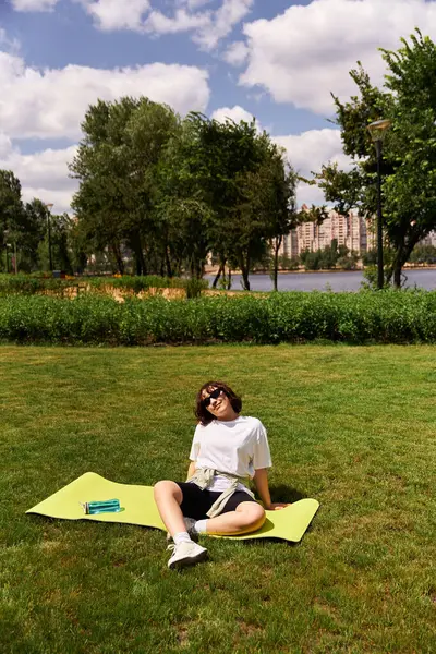 Young woman practices fitness stretches on a yoga mat beside a serene lake in a vibrant park. — Stock Photo
