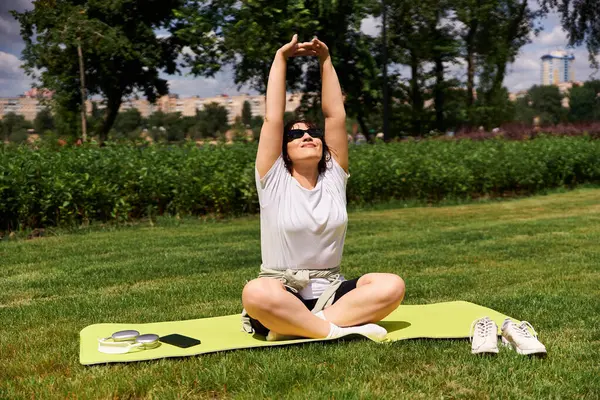 A fit young woman stretches peacefully outdoors on a sunny day surrounded by greenery. — Stock Photo