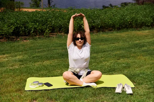 A fit young woman stretches on a yoga mat in a lively outdoor park, enjoying her workout. — Stock Photo