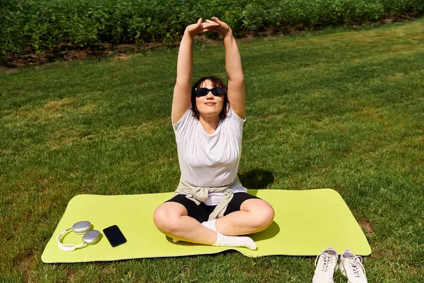 Pretty young woman stretches joyfully while sitting on a bright mat in nature. — Stock Photo
