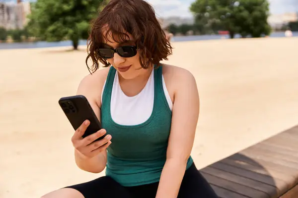 A young woman relaxes in the park, checking her phone while soaking up the summer sun. — Stock Photo