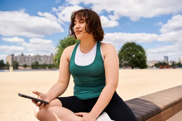 A young woman enjoys the sunshine while seated on a wooden bench, holding her phone. — Stock Photo