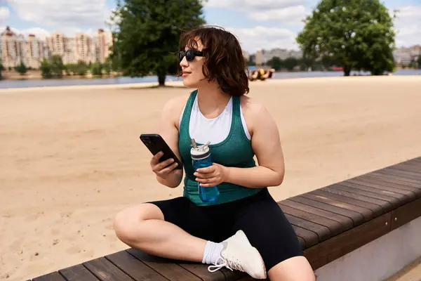 Una hermosa joven se relaja junto al agua, tomando una copa mientras disfruta del sol de verano. - foto de stock