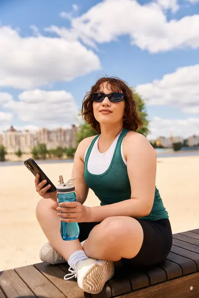 Smiling woman enjoys her time in the sun, seated on a bench with a drink in hand. — Stock Photo
