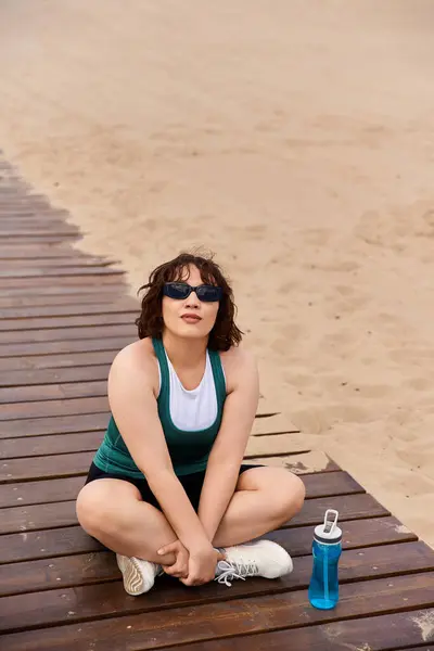A young woman stretches on the boardwalk after a beach workout, feeling refreshed. — Stock Photo