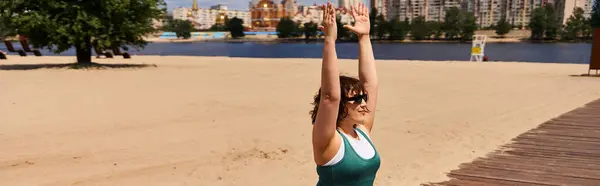 A young woman stretches her arms in a yoga pose on a sandy beach beside a calm river, banner — Stock Photo