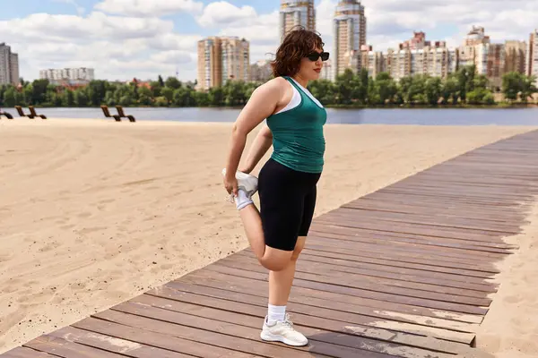 Une jeune femme en forme s'étend sur une promenade de plage, prête à faire de l'exercice sous un ciel dégagé. — Photo de stock