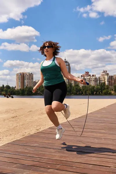 In forma giovane donna esercizi con una corda di salto su una bella spiaggia di sabbia sotto un cielo limpido. — Foto stock