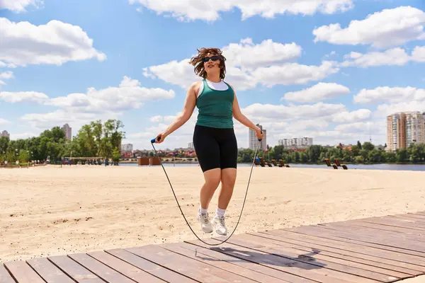 Young woman skips rope on sand, vibrant skyline behind her, enjoying fitness. — Stock Photo