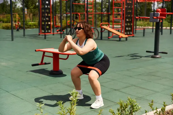 Young woman performs squats in a vibrant outdoor fitness area on a sunny day. — Stock Photo