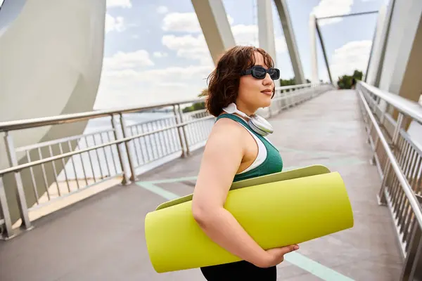 A pretty young woman walks confidently with a yoga mat, embracing the joy of outdoor exercise. — Stock Photo