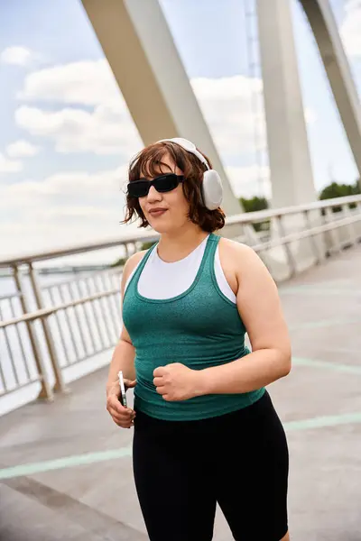 Young woman jogs on a scenic path, enjoying music with headphones in the sun. — Stock Photo