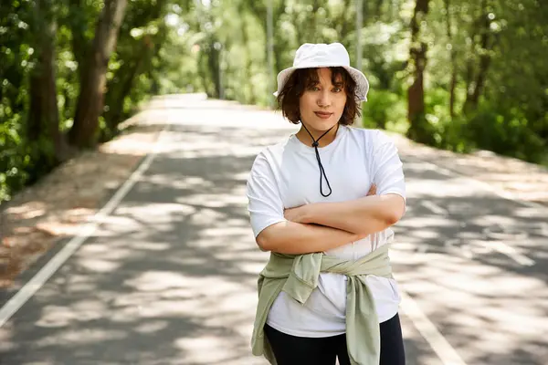 Smiling woman stands confidently outdoors, surrounded by lush green trees on a bright summer day. — Stock Photo