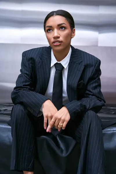 Mujer joven en traje de moda se sienta en una superficie elegante, mostrando su actitud hacia adelante de la moda. - foto de stock