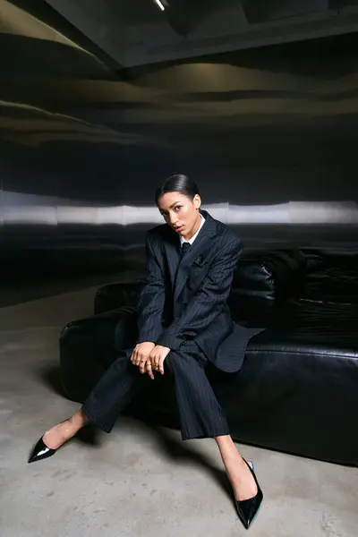 Jeune femme élégante pose gracieusement sur un canapé élégant, exsudant confiance et élégance. — Photo de stock