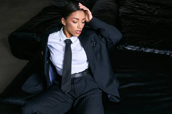 A fashionable young woman in elegant attire exudes confidence while seated on a plush couch. — Stock Photo
