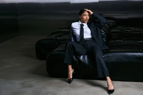Una joven vestida con estilo posa elegantemente en un sofá negro contemporáneo, exudando elegancia. - foto de stock