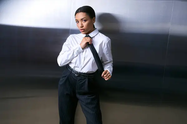 Vestida con un atuendo elegante, una mujer joven ajusta su corbata en un entorno urbano contemporáneo. - foto de stock