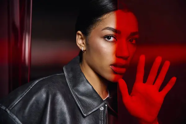 A stylish young woman in fashionable attire engages with a vibrant red backdrop, exuding elegance. — Stock Photo