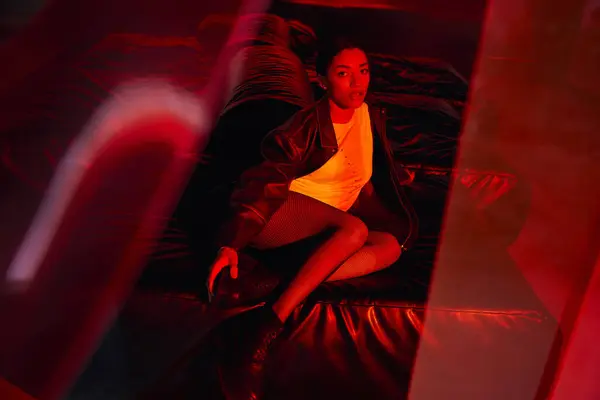Una mujer joven con estilo se destaca en su traje elegante, rojos vibrantes e iluminación dinámica. - foto de stock