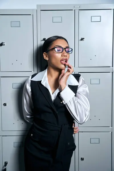 Mujer joven confiada en traje elegante posa pensativamente al lado de casilleros elegantes en luz brillante. — Stock Photo