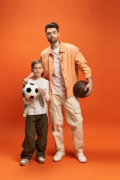 A joyful father and son holding a soccer ball and basketball, symbolizing togetherness and love. — Stock Photo