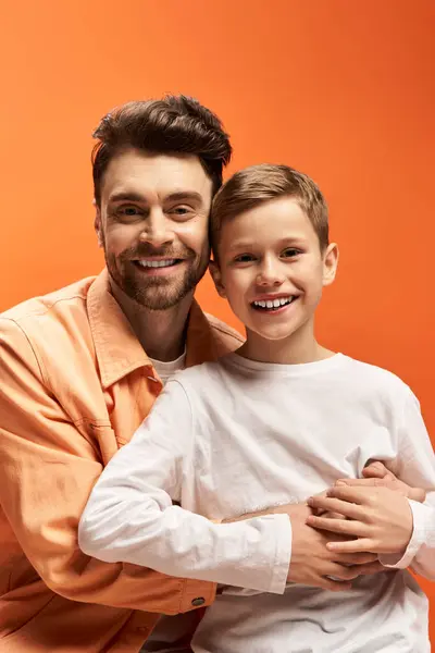 A joyful father hugs his son against a warm orange backdrop, celebrating Fathers Day. — Stock Photo