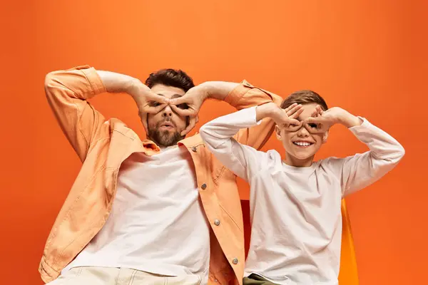 Vater und Sohn drücken ihre Verbundenheit mit spielerischen Gesten vor einem leuchtend orangen Hintergrund aus. — Stockfoto