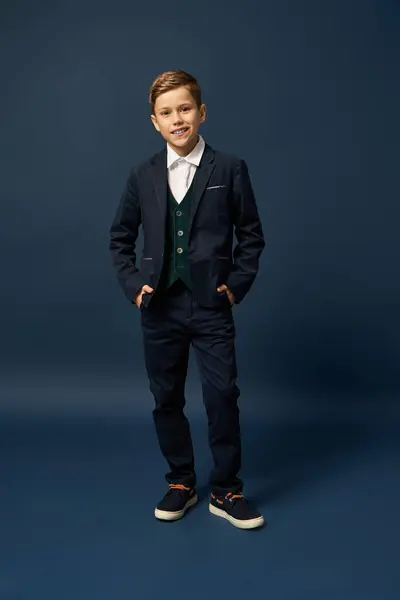A young boy dressed in a smart suit stands confidently on dark backdrop. — Stock Photo