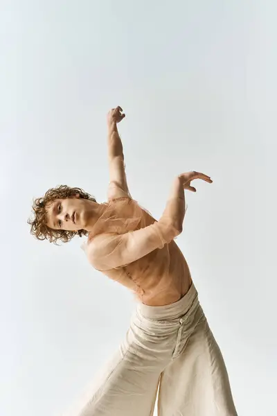 Un jeune homme aux cheveux bouclés met en valeur ses talents de danseur dans un contexte gris minimaliste. — Photo de stock
