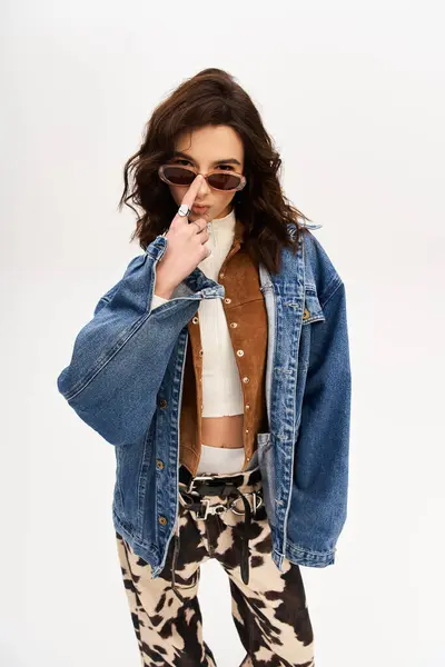 Stylish young woman poses confidently in cow print pants with a denim jacket and sunglasses. — Stock Photo