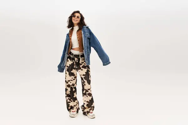 A young woman exudes confidence in cow print pants and a trendy jacket against a neutral backdrop. — Stock Photo