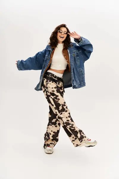 A fashionable young woman poses confidently in trendy cow print pants and oversized denim jacket. — Stock Photo
