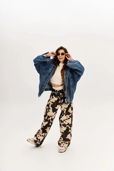 A fashionable woman wears cow print pants with a denim jacket against a minimalistic backdrop. — Stock Photo