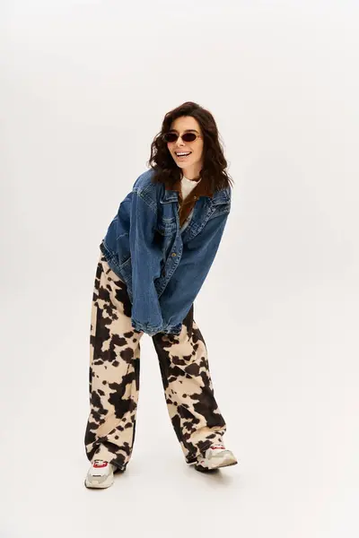 A young woman confidently poses in fashion-forward cow print pants and denim jacket, exuding style. — Stock Photo