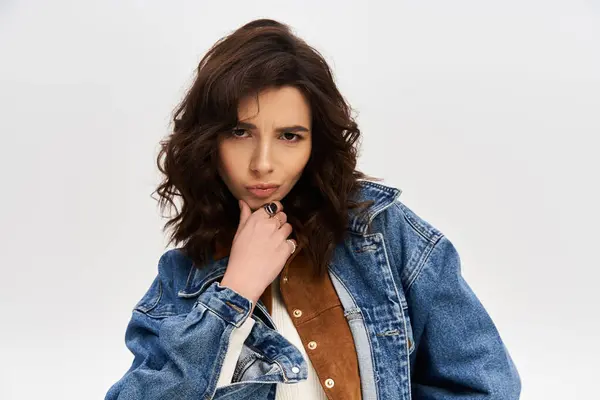 A young stylish woman showcases a trendy outfit against a grey backdrop. — Stock Photo