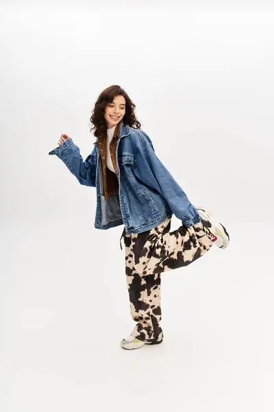 A young woman poses confidently in stylish cow print pants and denim jacket against a grey backdrop. — Stock Photo