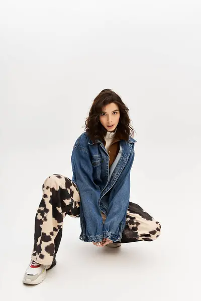 A young woman confidently poses in cow print pants and a denim jacket against grey. — Stock Photo