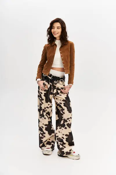 A young woman showcases her fashion sense with cow print pants and a chic top in a studio setting. — Stock Photo