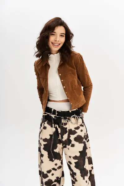 A young woman with a playful smile models a trendy outfit featuring cow print pants in a studio. — Stock Photo
