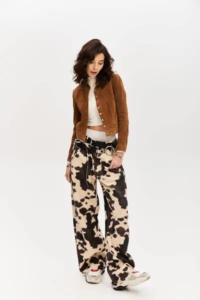 A young woman poses confidently in cow print pants and a chic jacket against a sleek grey backdrop. — Stock Photo
